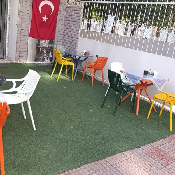 Kafe önündeki yuvarlak masaların çevresinde beyaz, yeşil, sarı ve turuncu plastik sandalye modelleri