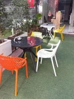 Yuvarlak siyah masa çevresinde turuncu ve beyaz kolçaklı, sarı kolçaksız plastik sandalyeler