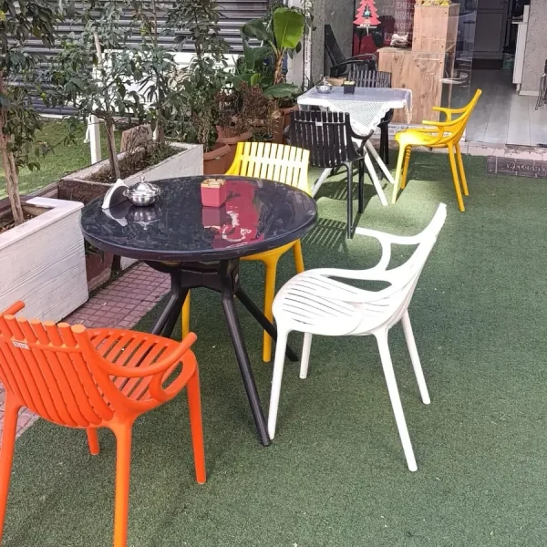 Yuvarlak siyah masa çevresinde turuncu ve beyaz kolçaklı, sarı kolçaksız plastik sandalyeler