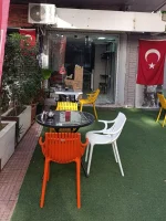 Kafe girişinde turuncu, beyaz ve sarı plastik sandalyelerle düzenlenmiş yuvarlak masalar